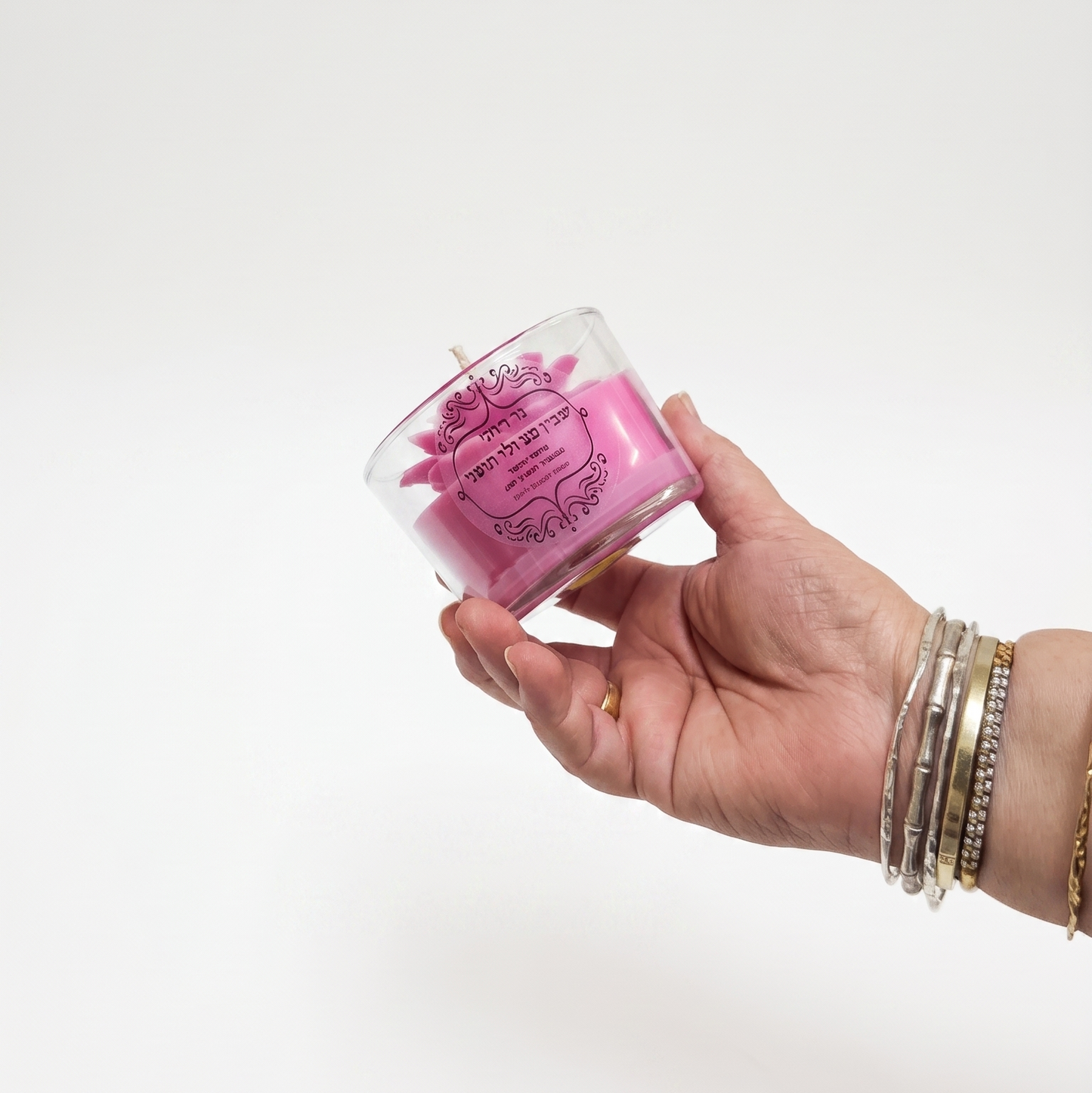 Hand holding a small glass container with pink contents against a white background