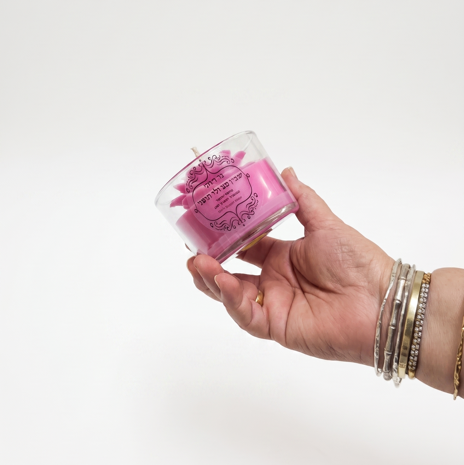 Hand holding a small glass container with pink contents against a white background